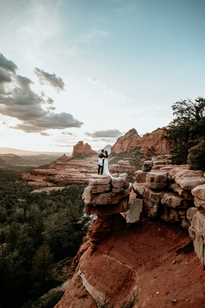 Eloping couple standing on a red rock cliff overlooking sunset taken Sedona elopement photographer Stratus Photography