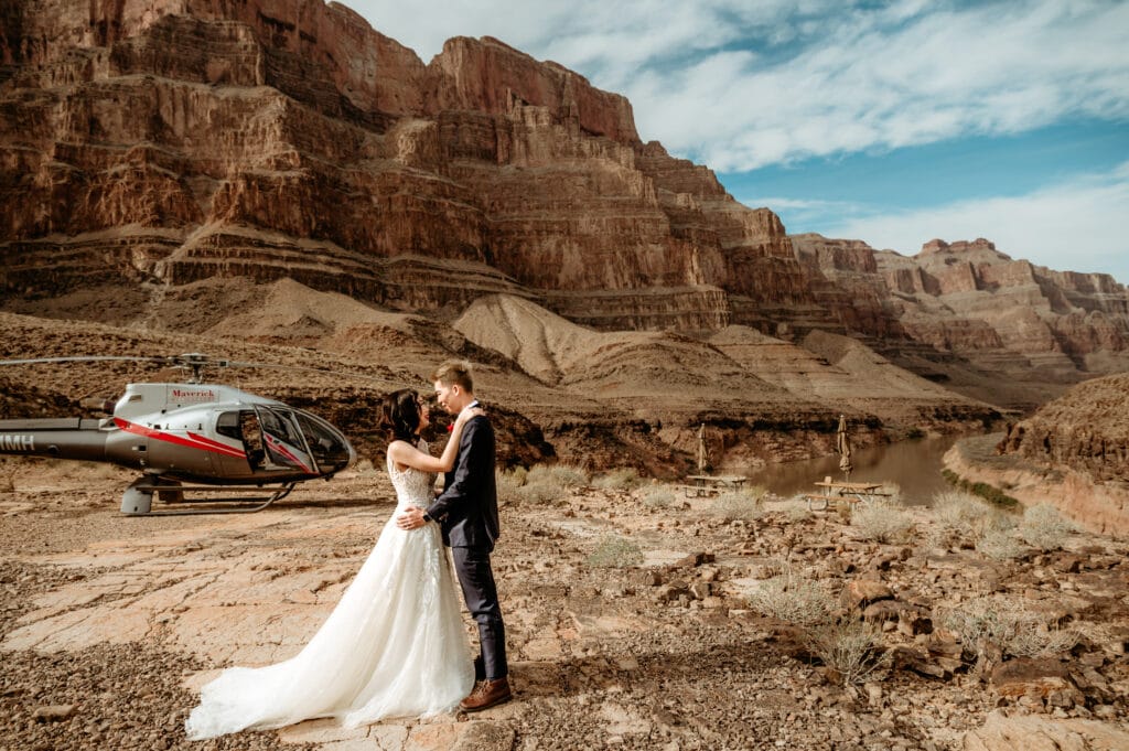 Bride and groom embrace with helicopter in the background during their Grand Canyon helicopter elopement