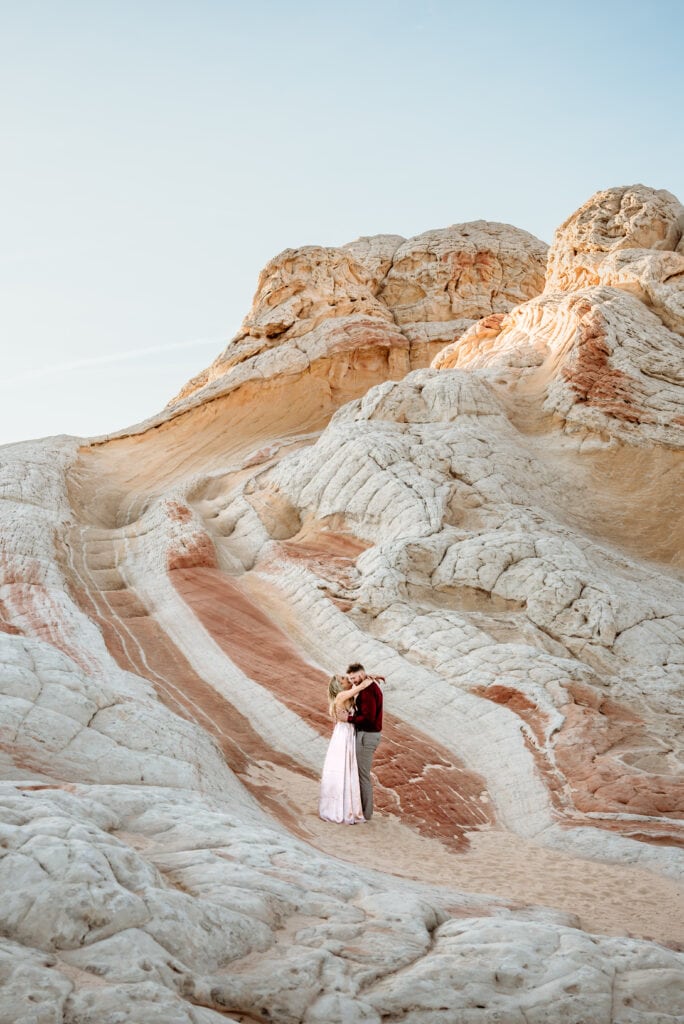 Couple embraces in the sand below one of the Vermillion Cliffs rock formations