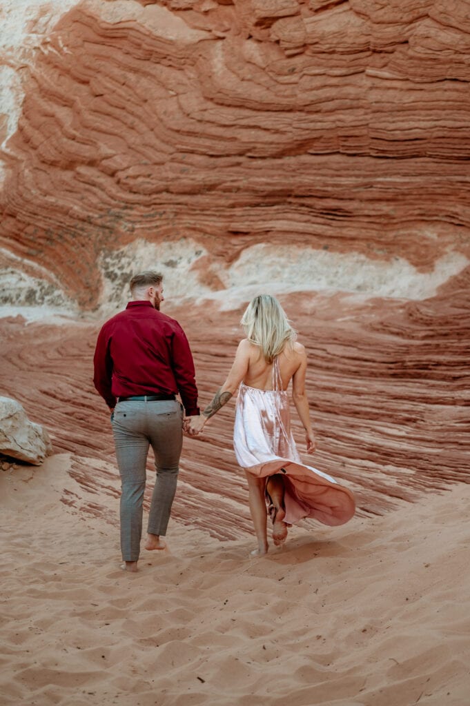 Shiny pink dress flows as couple walks barefoot in sand and red sandstone formations