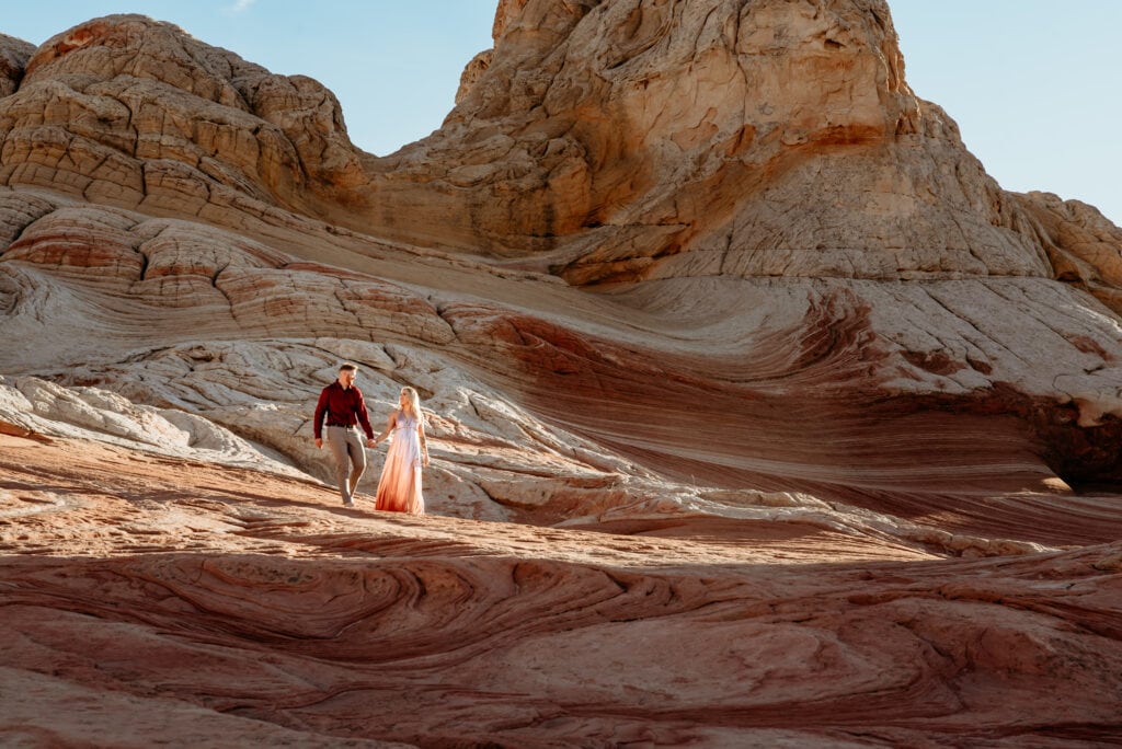 Cassie and Nick walking through wave formations of red and white sandstone