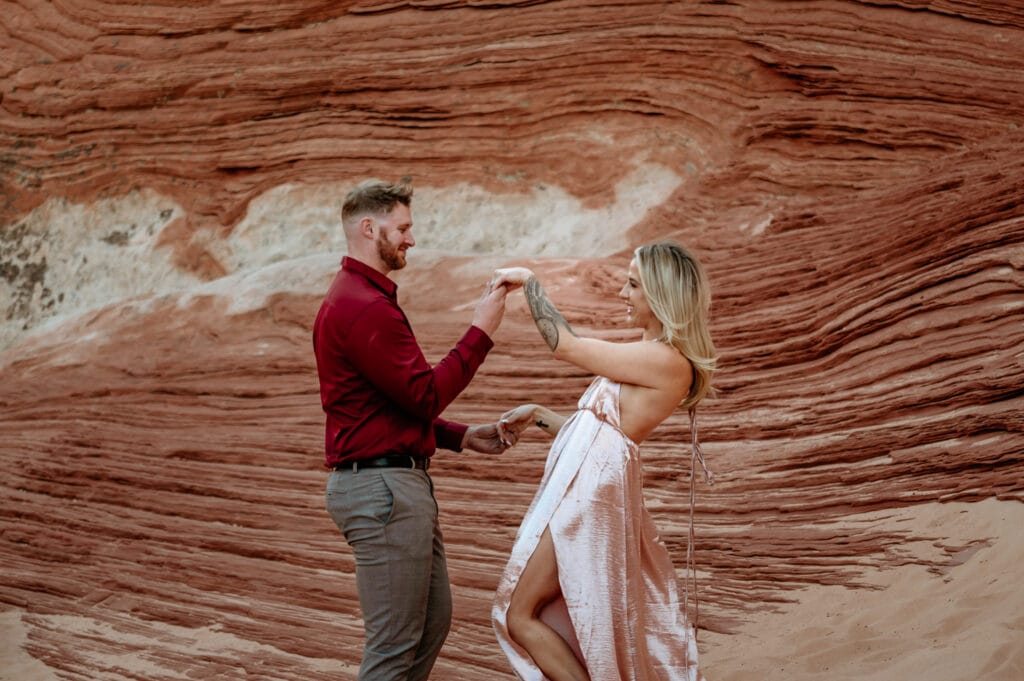Couple playfully holding hands and laughing surrounded by red sandstone layers