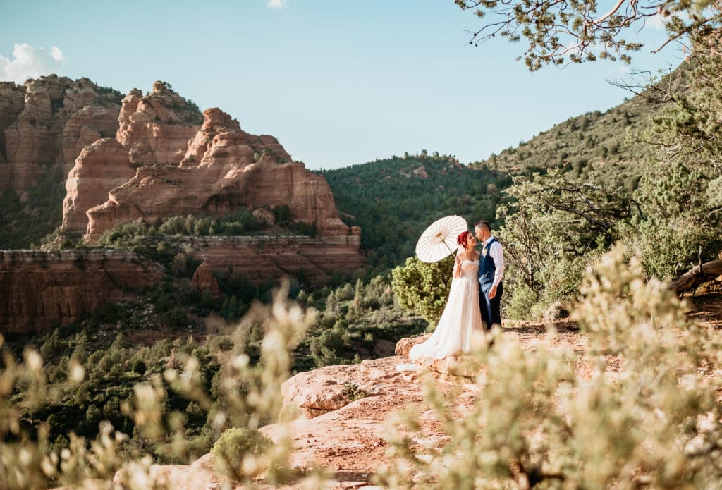 Couple standing on a red rock cliff with a parasol during their Sedona elopement