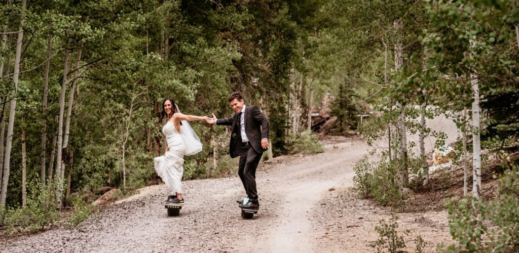 Bride and groom riding their one wheels down a gravel road surrounded by aspen trees taken by Arizona Elopement Photographer Shannon Durazo