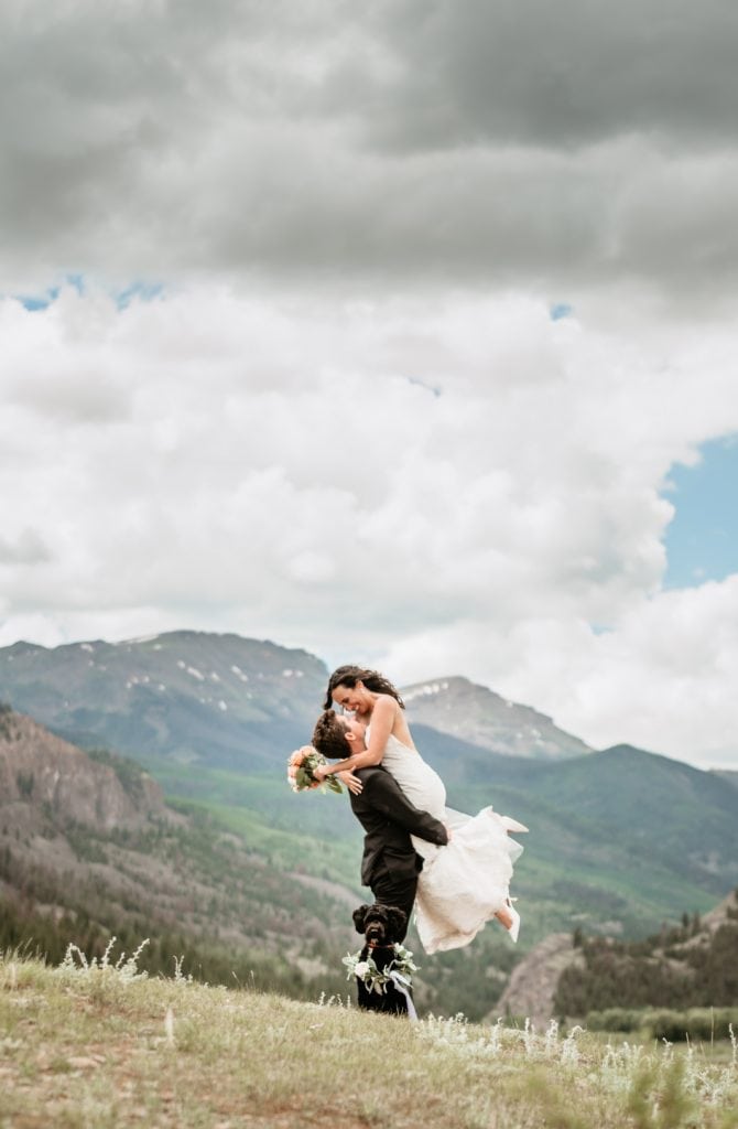 Groom lifting bride with their flower dog and Colorado mountains in the distance
