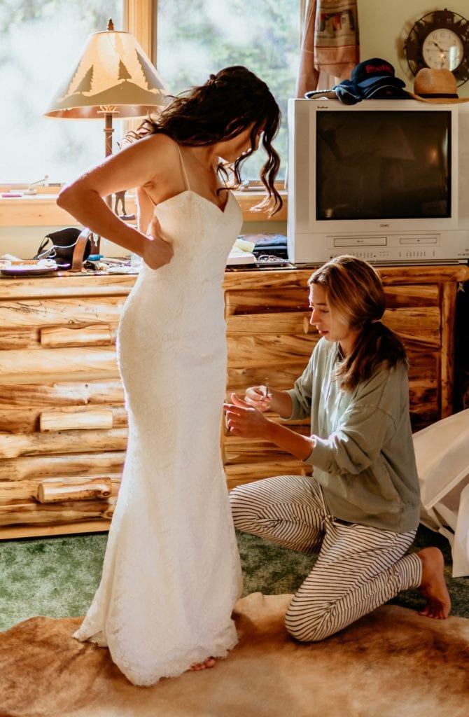 Best friend helping bride with dress the morning of her wedding