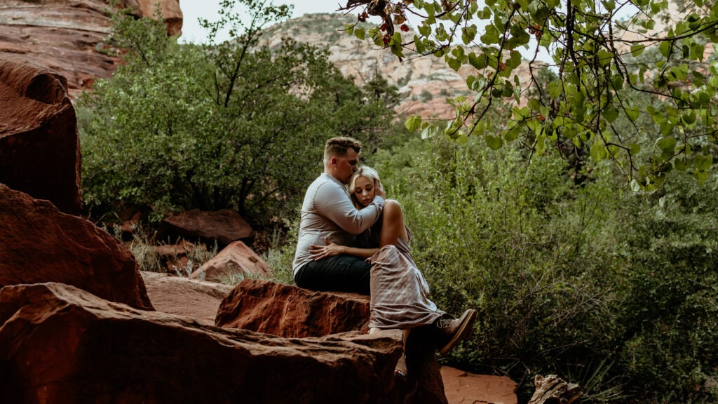 Couple embraces in a red rock wooded area in Sedona