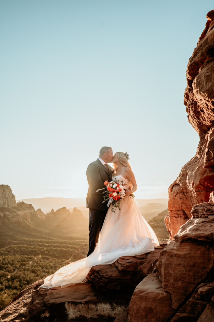 Wedding couple kiss enveloped by setting sun rays during their Sedona elopement