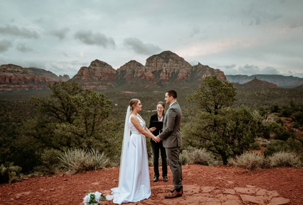 bride and groom hold hands as officiant reads ceremony during Sedona elopement wedding ceremony surrounded by red rock canyons