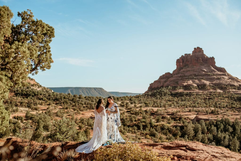 same sex couple saying their vows with views of Bell Rock in the distance during their Sedona elopement
